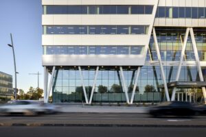 EPSYLON - Façade moderne d'un immeuble avec des voitures en mouvement au premier plan mettant en avant l'architecture contemporaine et le design urbain.