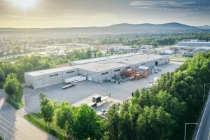 EPSYLON - Vue aérienne d'une usine moderne entourée de verdure avec une chaîne de montagnes à l'horizon sous un ciel ensoleillé au Québec Canada