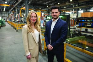 EPSYLON - Deux personnes en tenue professionnelle se tiennent dans une usine moderne avec des équipements industriels visibles en arrière-plan axés sur la production.